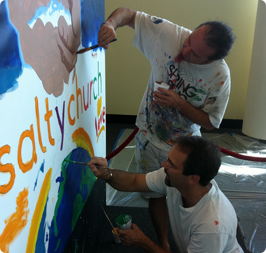 Two men painting a wall with white paint.